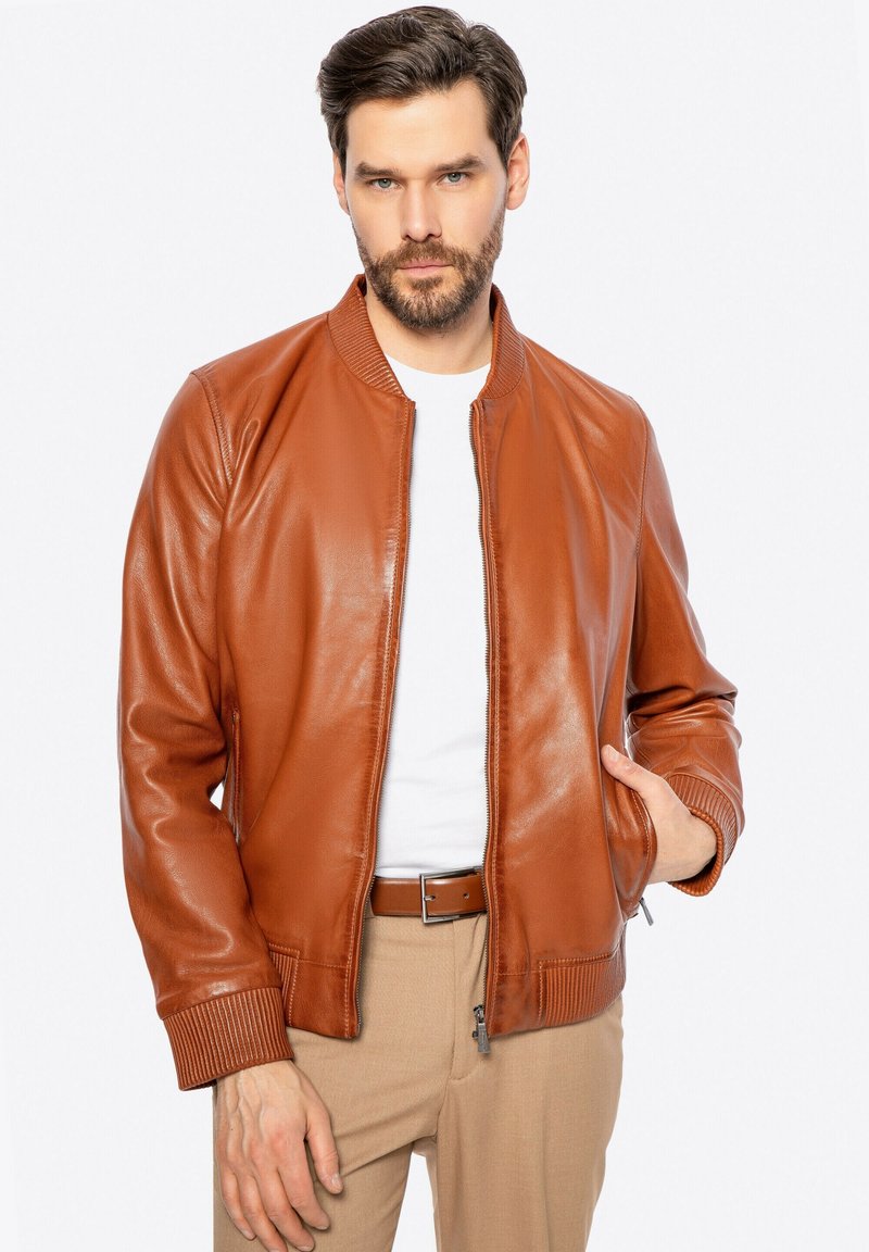 Giubbotto bomber in pelle marrone con colletto e polsini a costine, dotato di chiusura frontale con zip e tasche laterali. Texture liscia e colore caldo.