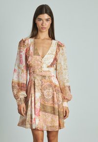 Krótka kwiatowa sukienka z długimi, bufiastymi rękawami, głębokim dekoltem w szpic, falbaniastymi akcentami i wzorzystym materiałem w odcieniach różu, beżu i złota.