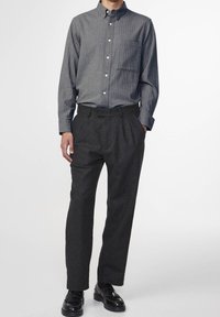 Button-up shirt in gray with subtle vertical stripes and pocket; paired with dark gray pleated trousers and black shoes.