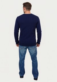 Marineblauwe geribbelde trui met lange mouwen en een ronde hals, gecombineerd met een blauwe spijkerbroek. De trui heeft een gestructureerd patroon en een aansluitende zoom.
