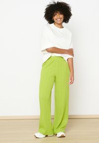 Zelene široke hlače s plisejem iz lahkega materiala, v kombinaciji z ohlapno belo majico. Bele superge dopolnijo outfit. Minimalističen dizajn.