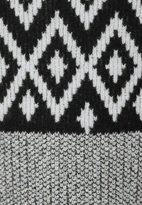 Stickad tyg med ett geometriskt diamantmönster i svart och vitt, med en texturerad grå kant längst ner.