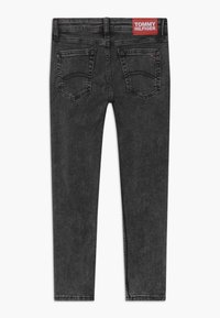 Jeans skinny negros con dos bolsillos traseros y un parche del logo rojo de Tommy Hilfiger en la cinturilla.