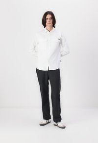 Chemise blanche à boutons avec deux poches poitrine, assortie à un pantalon gris foncé et des baskets avec des accents noirs et gris.