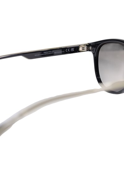 Gafas de sol con montura de plástico negro, lentes grises degradados y puntas de patilla blancas. Incluye logotipo y tecnología de lentes polarizados.