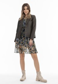 Grijze leren jas over een zwarte bloemenjurk met oranje en witte bloemen, gecombineerd met beige veterschoenen.