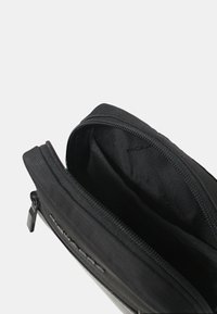 Pochette nera con zip realizzata in tessuto resistente, con una texture liscia e un design minimalista. Scomparto interno visibile, senza fantasie.