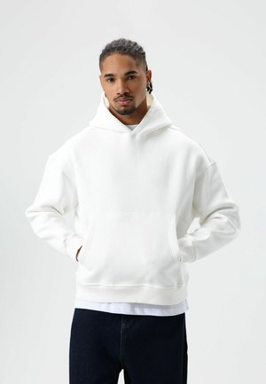 Witte hoodie gemaakt van zacht materiaal, met een kangoeroezak en geribbelde manchetten, gecombineerd met donkerblauwe spijkerbroek.