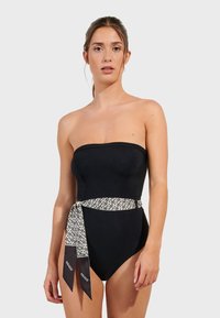 Svart bandeau-baddräkt med figursydd design, prydd med ett mönstrat bälte i en kontrasterande tyg som knyts i midjan.