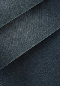 Tamni traper tkanina presavijena, prikazujući glatku teksturu s suptilnim twill uzorkom. Boja se kreće od duboke indiga do tamno plave.