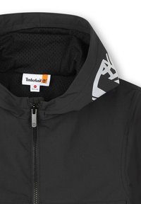 Giubbotto Timberland nero con zip frontale, fodera in rete e colletto con logo. Presenta un design minimalista e una texture liscia.