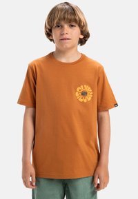 Bruine katoenen t-shirt met een circulair logo in het geel op de linkerkant van de borst. Korte mouwen, ronde hals, losse pasvorm. Gelaagd stof, glad oppervlak.