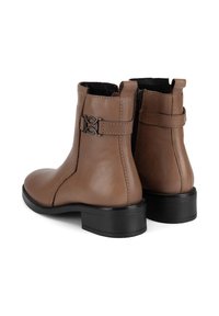 Brūnas ādas potītes zābaki ar gludu virsmu, melna gumijas zole un dekoratīva josta ar metāla akcentiem sānos.