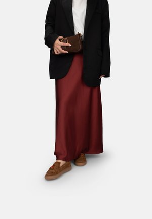 Schwarzer Blazer, weißes T-Shirt, burgunderfarbene Satin-Maxikleid, braune Wildlederschuhe mit Quasten, hält eine kleine braune Tasche mit einem runden Akzent.