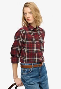 Rood- en marineblauw geruit overhemd met opgerolde mouwen, knoopsluiting aan de voorkant en twee borstzakken. Draagt het met een blauwe spijkerbroek en een bruine riem.