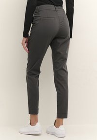 Grå skræddersyede bukser har høj talje, tætsiddende ben og baglommer, parret med hvide sneakers på en neutral baggrund.