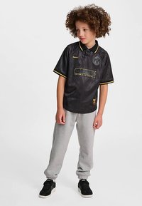 Svart kortärmad tröja i jersey med texturerad yta, gul kant och logodetalj framtill, kombinerad med gråa sweatpants och svarta sneakers.