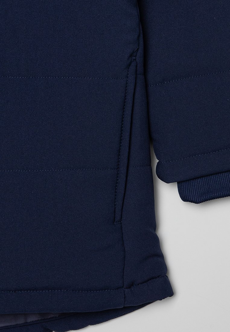 Veste isolée bleu marine avec texture matelassée, dotée d'une poche latérale et de poignets côtelés pour plus de chaleur et de confort.