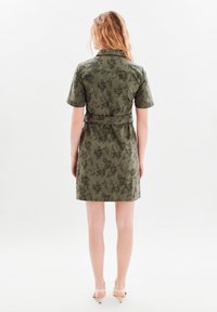 Abito verde oliva a maniche corte con stampa floreale, vita cinturata e collo. Tessuto liscio e design fino al ginocchio.