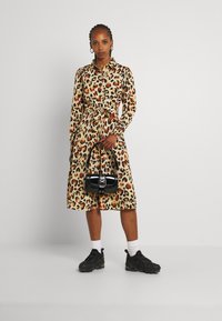 Vestido de estampa de leopardo com colarinho e faixa na cintura, em bege, laranja e preto; combinado com uma pequena mala preta e ténis Pretos.