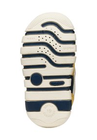 Suela de un zapato con un diseño ondulado en una base blanca y acentos azul marino. Goma texturizada con agujeros de ventilación y marca.