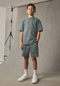 Graues Baumwoll-T-Shirt und passende Shorts, bequeme Passform, mit kurzen Ärmeln. Kombiniert mit weißen Turnschuhen und weißen, gerippten Socken.