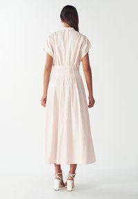 Vestido maxi de rayas en rosa claro, con mangas cortas, cintura elástica y corte relajado. Sandalias de tacón cuadrado blancas completan el look.