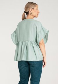 Miętowa bluzka peplum z luźnymi rękawami i marszczoną talią. Miękka tkanina o gładkiej fakturze. Połączona z ciemnoniebieskimi dżinsami.