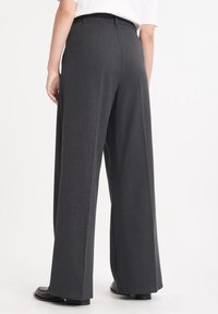 Vidbyxlningar i mörkgrått tyg, med en slät textur, skräddarsydd passform och sidofällar, kombinerat med svarta skor.