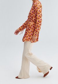 Colorful patterned button-up dress with a drawstring waist, paired with cream flared trousers and brown heeled shoes. Smooth fabric texture.