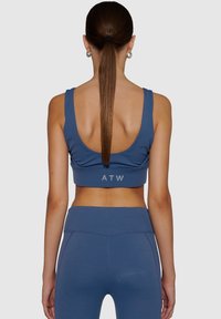 Blå sport-BH med låg ryggdesign, tjocka axelremmar och logodetalj "ATW" i en kontrasterande grå färg vid bandet. Mjuk, elastisk tyg.