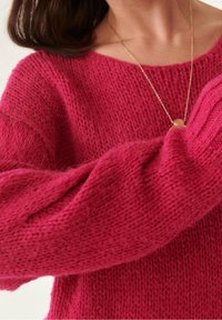 Suéter de punto oversize en fucsia con puños y cuello acanalados. Textura suave con un corte holgado, que muestra un diseño en capas y acogedor.