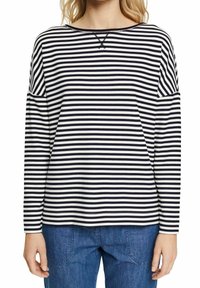 Top a maniche lunghe a righe in cotone blu navy e bianco, con scollo a barca, vestibilità rilassata e spalle scese. Jeans in denim blu visibili.