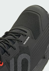 Czarny but sportowy wykonany z siateczki i gumowych materiałów. Posiada teksturowane akcenty, sznurowadła oraz etykietę "TRAILCROSS" z boku.