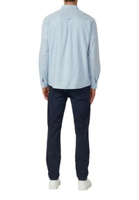 Jasnoniebieska koszula z długim rękawem i detalem na karku, zestawiona z ciemnoniebieskimi dżinsami i białymi trampkami, prezentująca casualowy styl.