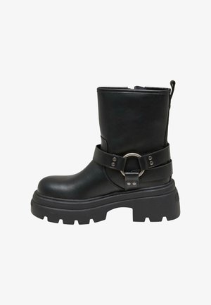 Botín de cuero negro hasta el tobillo con suela gruesa, que presenta una correa con un acento de anillo plateado. Textura suave, punta redondeada y tirador en la parte posterior.