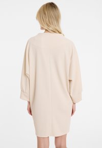 Hellbeige Oversized-Kleid mit Fledermausärmeln, glatter Textur und schlichter Gestaltung. Zu den wichtigsten Merkmalen gehören eine rückwärtige Naht und umgeschlagene Bündchen.