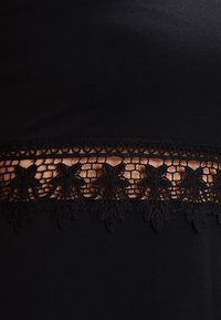 Černá tkanina s jemným černým krajkovým lemem s květinovými vzory a vlnitými okraji. Hladká textura s přiléhavým střihem.