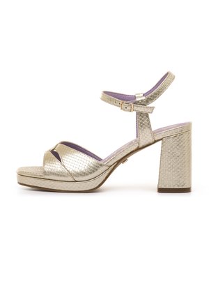 Sandalia metálica dorada con tacón de bloque, correa en el tobillo con hebilla, patrón texturizado de serpiente y forro interior púrpura.