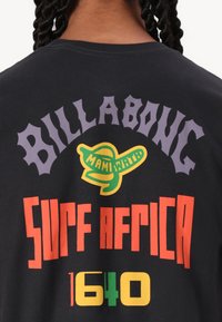 Zwarte katoenen t-shirt met kleurrijke graphic tekst: "BILLABONG," "MAMINATI," "SURF AFRICA," en "1640," in verschillende lettertypes en kleuren.