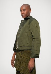 Pehmea roheline bomber jaki, millel on lukuga esiosa, elastsed mansetid ja tõmbestringiga alläär. Omab peent geomeetrilist mustrit ja logopatchi.