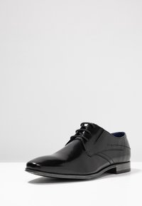 Chaussure habillée en cuir noir avec une finition polie, bout pointu et fermeture à lacets. Présente un logo discret et un intérieur bleu contrastant.