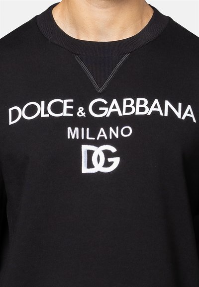 Zwarte sweatshirt met daarop "Dolce & Gabbana Milano" in witte tekst en een grijs geborduurd "DG"-logo. Textuur bij de halslijn met ribgebreide accenten.