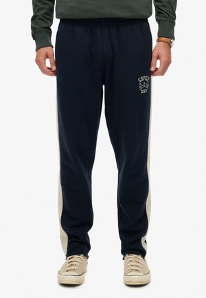 Navy blue joggers made of soft fabric with a white side panel and embroidered logo detail. Features an elastic waistband and tapered fit.