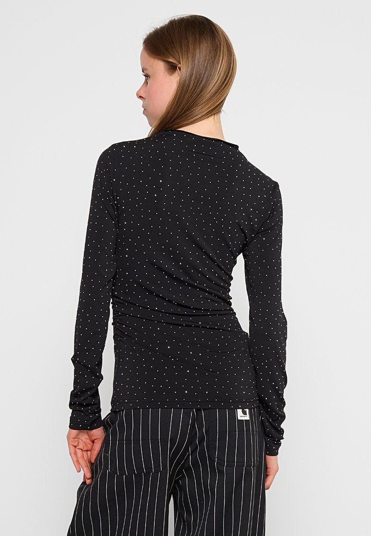 Maglietta nera a maniche lunghe con piccoli pois bianchi, tessuto morbido, design aderente e dettaglio arricciato sul retro. Abbinata a pantaloni a righe.