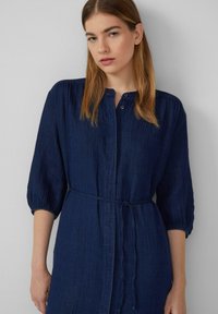 Abito button-up blu scuro, testurizzato, con maniche a tre quarti e vita legata. Presenta cuciture sottili e una vestibilità comoda.