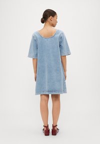 Vestido de denim azul claro com mangas curtas e decote arredondado. Apresenta costura visível e uma silhueta reta, terminando acima do joelho.
