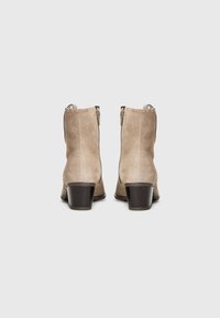 Botine din suede bej, cu vârful rotunjit, toc din lemn maro de tip bloc și închidere cu fermoar pe lateral, având detalii cu cusătura.