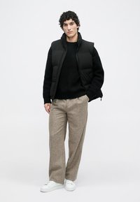 Chaleco acolchado negro sobre un suéter de punto negro, combinado con pantalones de pierna ancha beige y zapatillas blancas. Diseño sencillo, texturas suaves.