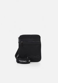 Svart Valentino crossoverväska med framfickor med dragkedja och justerbar axelrem med varumärke, visad mot vit bakgrund.